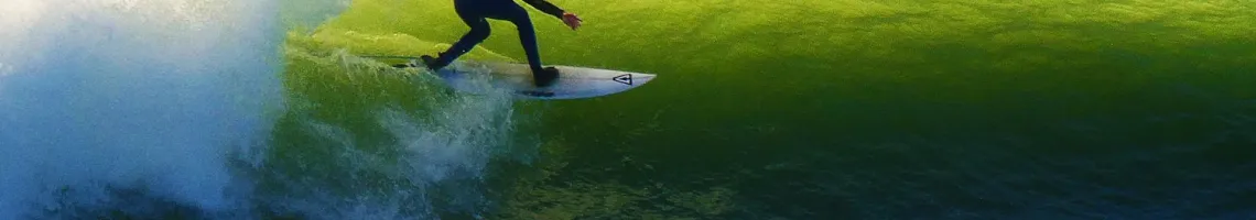 Surfer riding a green wave with white spray in blue ocean waters